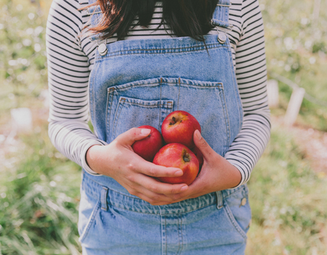 Woman holding three red apples in front of her stomach